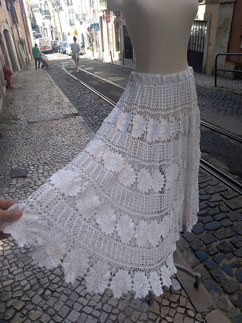 May include: A white crochet skirt with a floral design. The skirt is long and flowing, and it has a delicate lace trim.