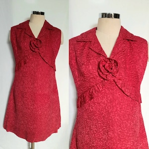 May include: A sleeveless red dress with a textured fabric and a large red flower accent on the bodice. The dress has a V-neckline and a collar.