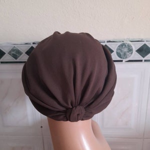 May include: A brown turban style head wrap made of soft fabric. The wrap is tied at the back of the head.