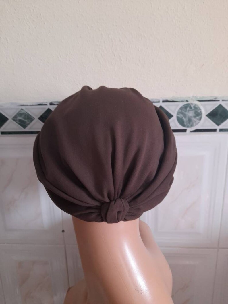 May include: A brown turban style head wrap made of soft fabric. The wrap is tied at the back of the head.