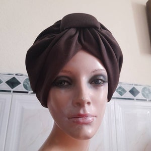 May include: A brown turban style hat with a knot on top. The hat is made of a soft, fabric material.