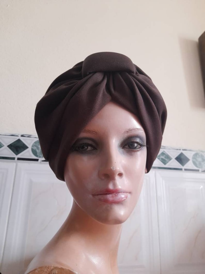 May include: A brown turban style hat with a knot on top. The hat is made of a soft, fabric material.