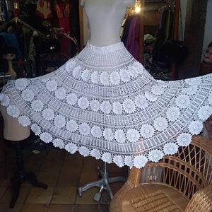 May include: A white crocheted skirt with a floral design. The skirt is full and flowing, and it is made with delicate crochet stitches.