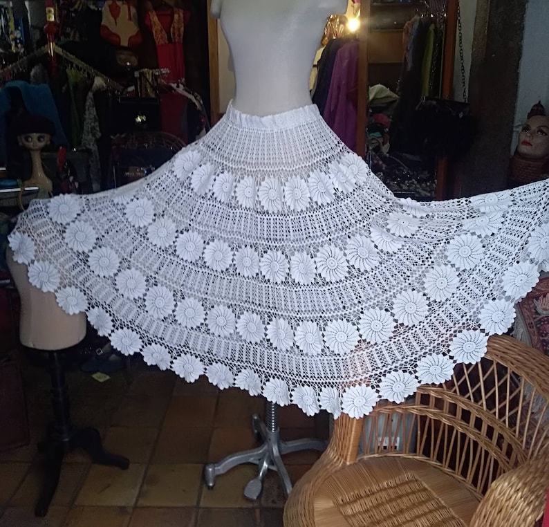 May include: A white crocheted skirt with a floral design. The skirt is full and flowing, and it is made with delicate crochet stitches.