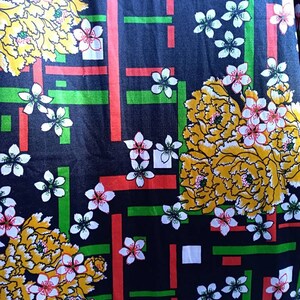 Pode incluir: Tecido preto com um padr&atilde;o repetido de flores amarelas e brancas, listras vermelhas e verdes e quadrados brancos.