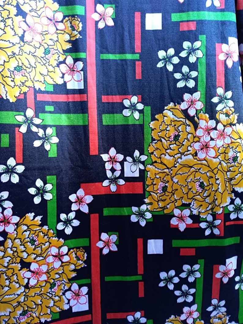 Pode incluir: Tecido preto com um padr&atilde;o repetido de flores amarelas e brancas, listras vermelhas e verdes e quadrados brancos.