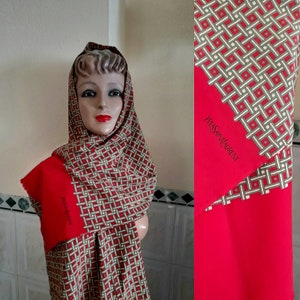 May include: A red and green patterned silk scarf with the text "Yves Saint Laurent" printed on the red side. The scarf is folded and draped around a mannequin's neck.