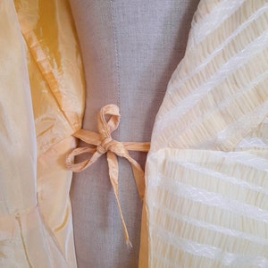 May include: A yellow sheer fabric with a white striped pattern. The fabric is tied with a yellow ribbon at the waist.