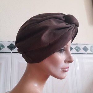 May include: A brown turban style hat with a knot on top. The hat is made of a soft, smooth fabric.
