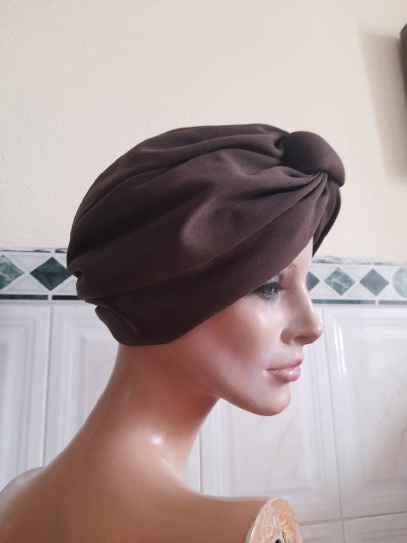 May include: A brown turban style hat with a knot on top. The hat is made of a soft, smooth fabric.