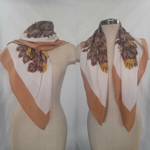 May include: A white silk scarf with a brown and yellow floral pattern. The scarf has a brown border and is displayed on a white mannequin.