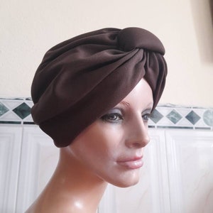 May include: A brown turban style hat with a knot on top. The hat is made of a soft, smooth fabric.