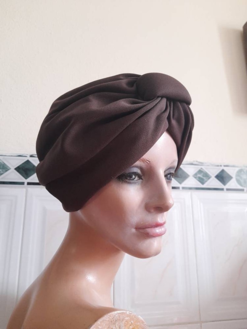 May include: A brown turban style hat with a knot on top. The hat is made of a soft, smooth fabric.