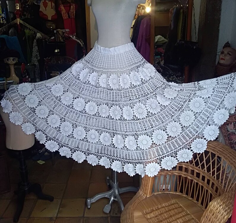 May include: White crochet skirt with a floral design. The skirt is full and flowing, and it is made of delicate crocheted lace.
