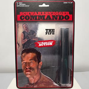 May include: Action figure packaging for the movie Commando, featuring Arnold Schwarzenegger. The packaging is red and black with the words "Schwarzenegger Commando" and "The Pipe". The figure is for ages 17 and up.