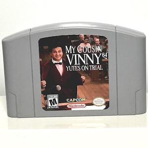 May include: A gray Nintendo 64 video game cartridge featuring the game "My Cousin Vinny 64: Yutes on Trial." The label shows a man in a suit and bow tie. The game is rated M for Mature.