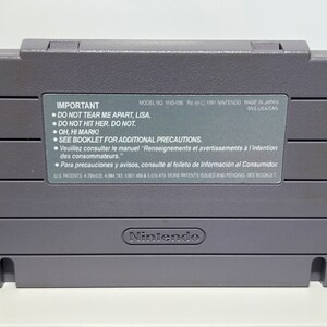 K&ouml;nnte beinhalten: Eine graue Super Nintendo Entertainment System (SNES) Spielkassette mit dem Text "IMPORTANT" und einer Liste von Warnhinweisen. Die Kassette tr&auml;gt das Nintendo-Logo unten.