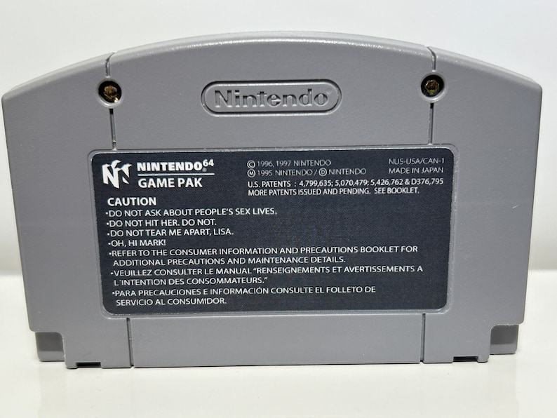 K&ouml;nnte beinhalten: Eine graue Nintendo 64-Spielkassette mit einem schwarzen Etikett. Das Etikett zeigt das Nintendo 64-Logo, die Worte "Game Pak" und eine Warnmeldung. Der Text auf dem Etikett enth&auml;lt Copyright-Informationen, Patentnummern und Anweisungen, um sich auf die Verbraucherinformationen und Vorsichtsma&szlig;nahmen im Booklet zu beziehen.