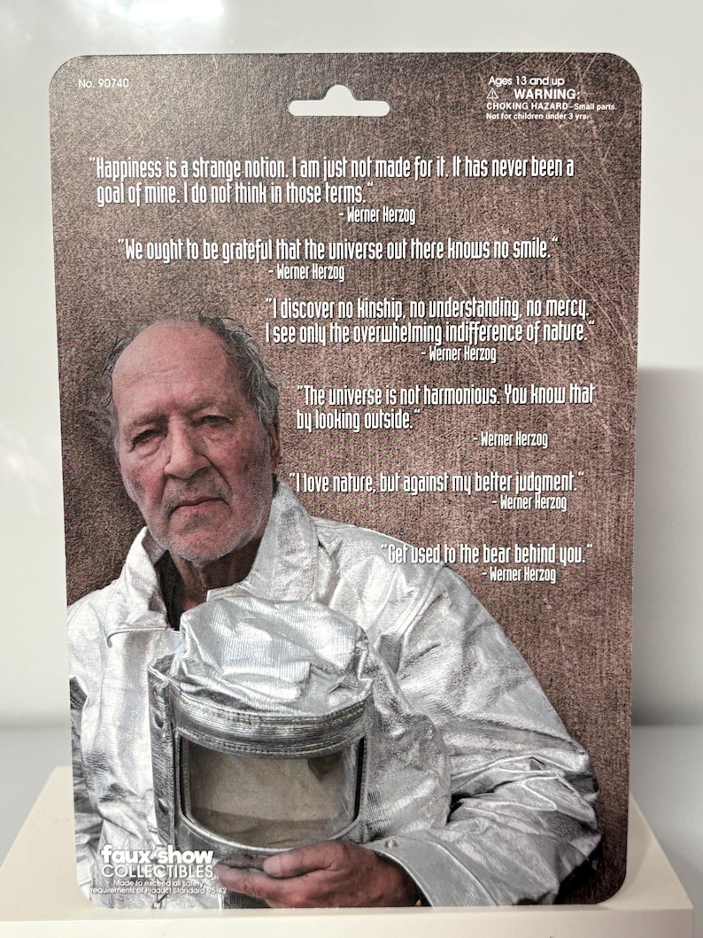 K&ouml;nnte beinhalten: Eine Sammelkarte mit einem Portr&auml;t von Werner Herzog und ihm zugeschriebenen Zitaten. Die Karte hat eine silberfarbene Metallic-Oberfl&auml;che und enth&auml;lt den Text "faux show COLLECTIBLES". Die Karte ist f&uuml;r Personen ab 13 Jahren geeignet.