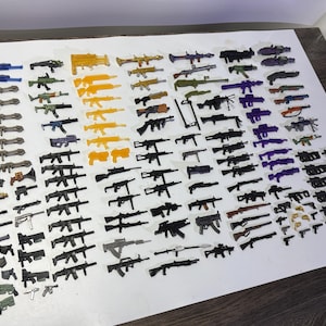 May include: A large collection of miniature toy weapons including various rifles, pistols, and heavy artillery pieces in assorted colors such as black, grey, orange, purple, and green, arranged in rows on a white surface for display.