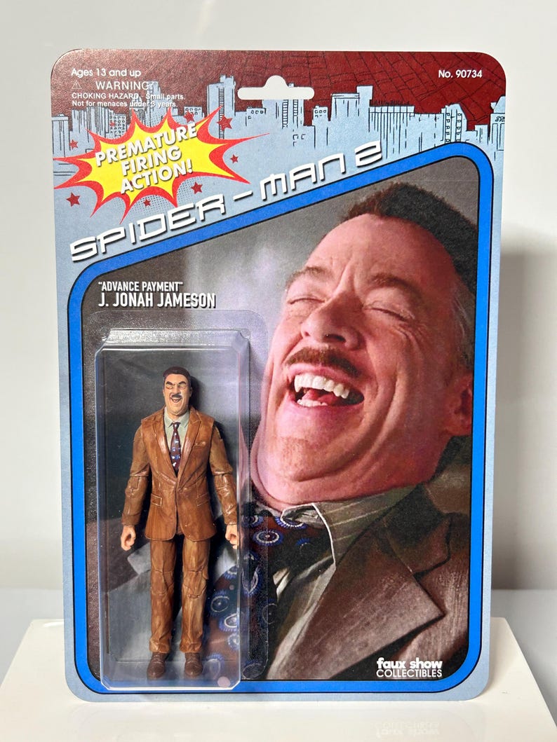Pu&ograve; includere: Action figure di Spider-Man 2 di J. Jonah Jameson in abito marrone, confezionata su una carta in stile retr&ograve;. La carta presenta una grande immagine di Jameson che ride, con il testo "PREMATURE FIRING ACTION!" e "ADVANCE PAYMENT". La confezione &egrave; etichettata "faux show COLLECTIBLES".