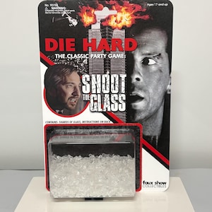 K&ouml;nnte beinhalten: Die Hard The Classic Party Game Shoot The Glass in Original-Blisterverpackung. Die Karte zeigt ein schwarz-wei&szlig;es Bild von zwei M&auml;nnern, ein brennendes Geb&auml;ude und den Titel in rotem und wei&szlig;em Text. Ein durchsichtiger Kunststoffbeh&auml;lter enth&auml;lt klare Glassplitter.