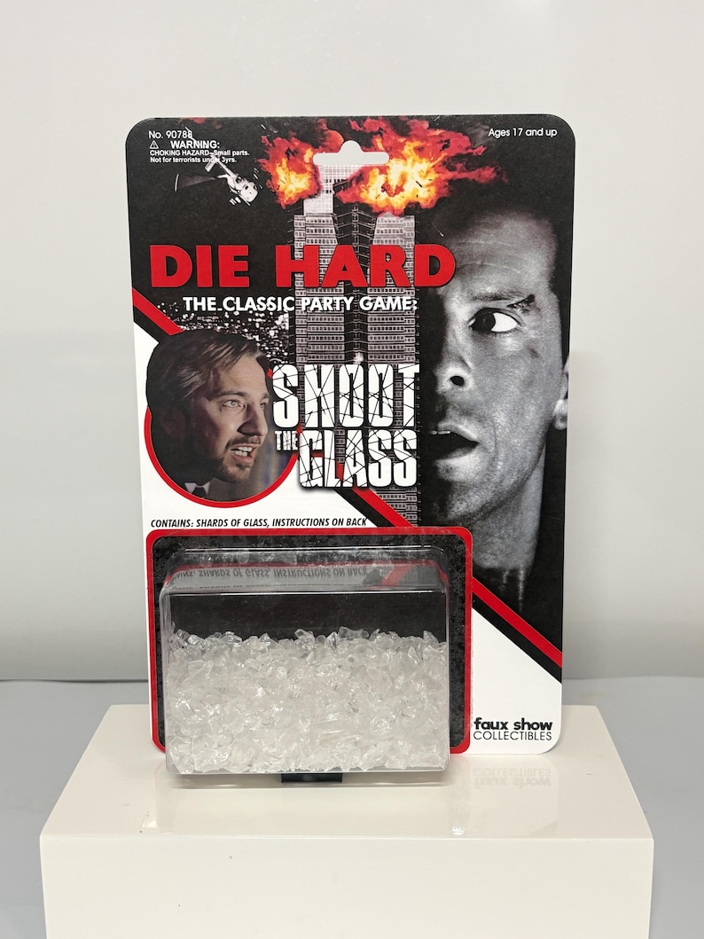 K&ouml;nnte beinhalten: Die Hard The Classic Party Game Shoot The Glass in Original-Blisterverpackung. Die Karte zeigt ein schwarz-wei&szlig;es Bild von zwei M&auml;nnern, ein brennendes Geb&auml;ude und den Titel in rotem und wei&szlig;em Text. Ein durchsichtiger Kunststoffbeh&auml;lter enth&auml;lt klare Glassplitter.