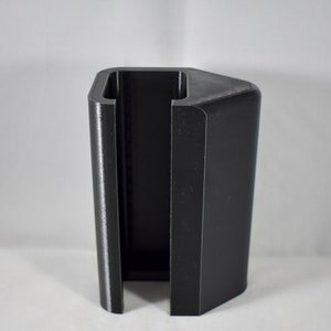 May include: A black plastic phone stand with a rectangular shape and a slot for holding a phone.