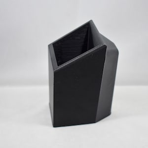 May include: A black plastic organizer with a slanted top opening. The organizer is designed to hold items upright.