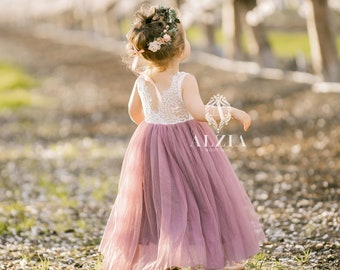 May include: A young girl wearing a mauve tulle dress with a white lace bodice and a flower crown. She is standing in a field of blooming trees.