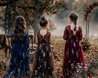 Può includere: Tre abiti lunghi fino ai piedi in blu navy, marrone e bordeaux, ciascuno con maniche lunghe in pizzo, scollo a V sulla schiena e gonna in tulle decorata con delicati ricami floreali, indossati da tre persone in un campo di foglie autunnali.