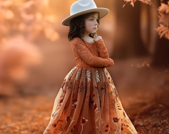May include: A young person wearing an orange lace dress with floral embroidery and a white hat. The dress has long sleeves and a flowing skirt. The background is a blurred outdoor scene with warm, autumnal colors.