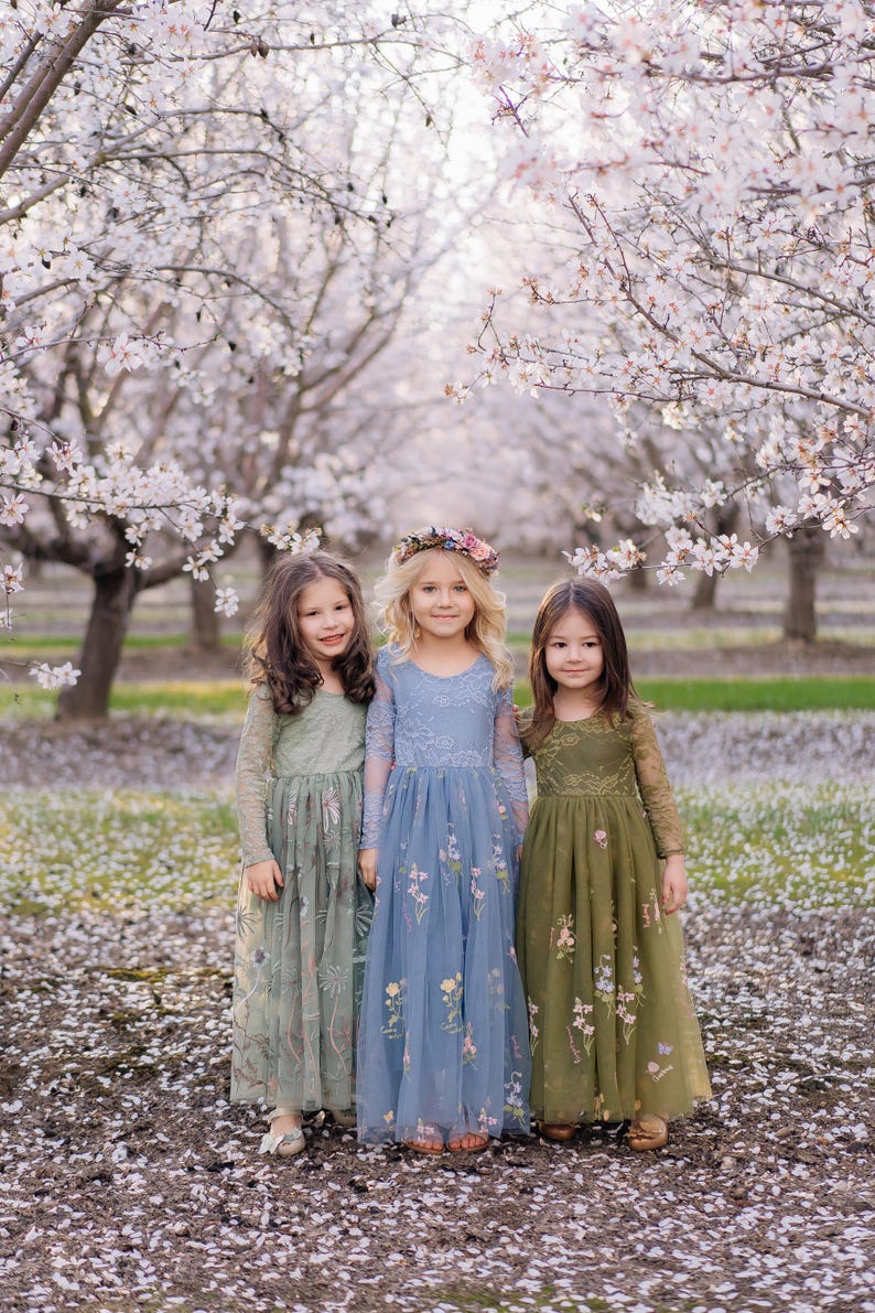 Pu&ograve; includere: Tre abiti a maniche lunghe fino ai piedi in verde salvia, blu polvere e verde oliva. Ogni abito presenta uno scollo rotondo, un corpetto aderente con dettagli in pizzo e una gonna in tulle fluida decorata con motivi floreali ricamati.