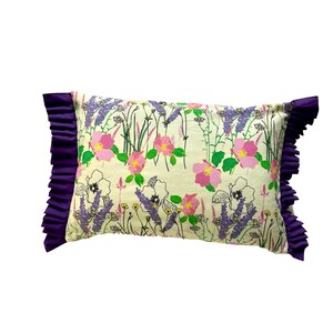 Puede incluir: Una almohada blanca con estampado floral de rosas rosas y lavanda morada. La almohada tiene un ribete morado con volantes.