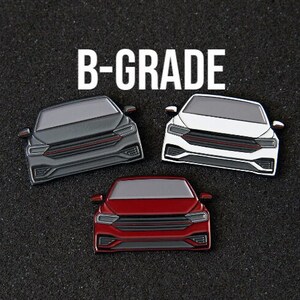 以下が含まれることがあります： 黒、白、赤の車の形をした3つのエナメルピン。黒いテクスチャの表面に配置されています。各ピンは、赤いアクセントが付いた詳細な車のデザインが特徴です。「B-GRADE」という単語が白い文字で表示されています。