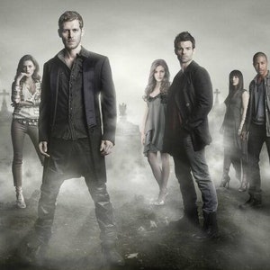 May include: Group photo of nine people, likely actors, in dark clothing, standing in a foggy graveyard setting. The image has a dramatic, gothic aesthetic, with a focus on the characters' expressions and attire.