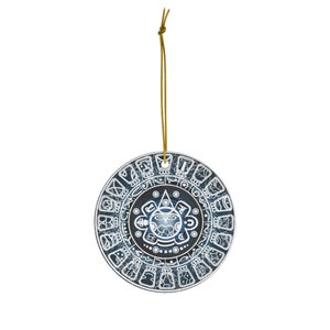 May include: A circular ornament with a Mayan calendar design in blue and white. It has a gold hanging string. The central design features a sun face, surrounded by glyphs and symbols. The ornament is approximately 10 cm in diameter.