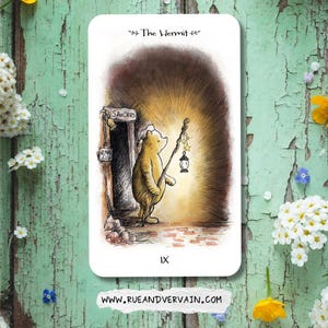 May include: A rectangular tarot card featuring a watercolor illustration of a yellow bear holding a staff with a hanging lantern and stars. The text reads The Hermit, IX, and Sanders. The background shows a dark doorway with a warm, glowing light.