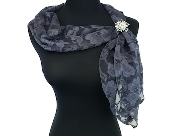 Könnte beinhalten: Dunkelgrauer Spitzenschal auf einer Schaufensterpuppe. Der Schal wird von einer silberfarbenen Brosche mit floralem Design und Perlenakzenten gehalten. Das Spitzenmuster zeigt ein Blumenmotiv, das dem Accessoire Eleganz verleiht.
