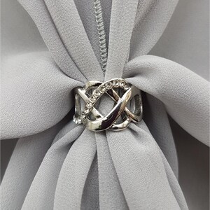 Puede incluir: Pin para hiyab de plata con un dise&ntilde;o de nudo decorativo y diamantes de imitaci&oacute;n transparentes.