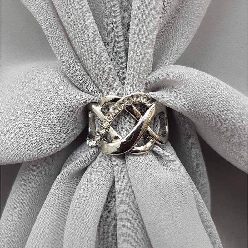 Puede incluir: Pin para hiyab de plata con un dise&ntilde;o de nudo decorativo y diamantes de imitaci&oacute;n transparentes.