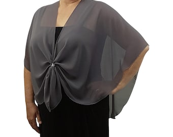 May include: A grey chiffon shawl with a V-neck design. The shawl is secured at the front with a decorative clasp. The garment is draped over a black dress, creating an elegant silhouette. The shawl is a versatile accessory, suitable for various occasions.