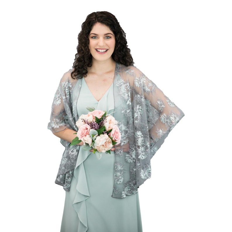 K&ouml;nnte beinhalten: Eine Frau in einem hellblauen Kleid mit einem grauen Spitzen-Schal und einem Strau&szlig; rosa und wei&szlig;er Blumen.
