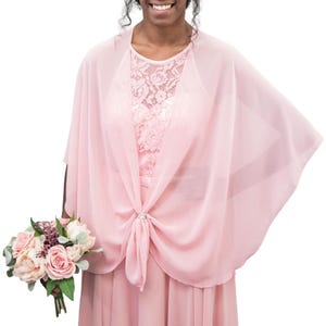 May include: A light pink chiffon shawl tied at the front with a decorative clasp. The shawl is draped over a pink lace bodice dress. A bouquet of pink and white flowers is held in the left hand.