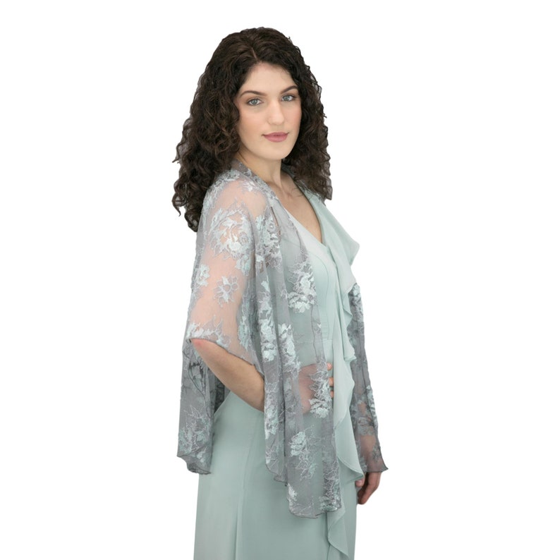 K&ouml;nnte beinhalten: Ein hellblauer Spitzen-Schal mit Blumenmuster. Der Schal ist &uuml;ber die Schultern einer Frau gelegt und bedeckt teilweise ein hellblaues Kleid.