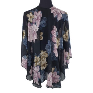 May include: A black floral cape with a sheer, flowing design. The cape features large, detailed flowers in shades of pink, blue, and tan. The cape is displayed on a black mannequin, showcasing its shape and drape.
