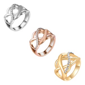 Puede incluir: Tres anillos en plata, oro rosa y oro. Cada anillo presenta un dise&ntilde;o de s&iacute;mbolo de infinito con una fila de peque&ntilde;as piedras preciosas transparentes. Los anillos se muestran sobre un fondo blanco.