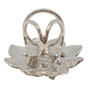 K&ouml;nnte beinhalten: Silberner Ringhalter mit floralem Design. Der Halter hat die Form einer Blume mit einer zentralen &Ouml;ffnung f&uuml;r einen Ring.