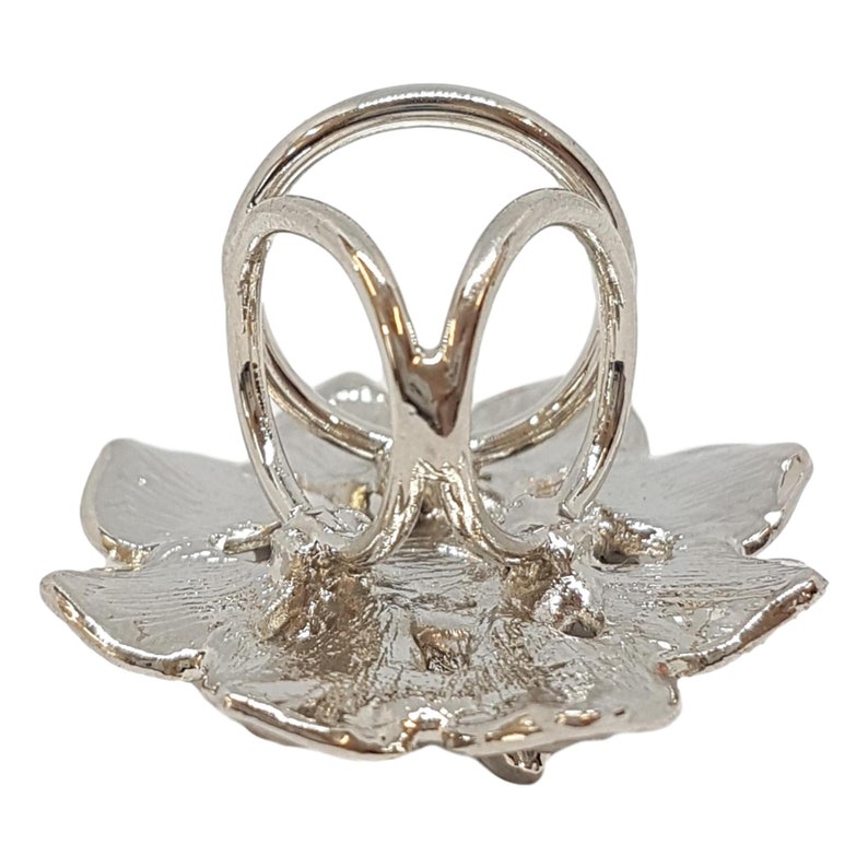 K&ouml;nnte beinhalten: Silberner Ringhalter mit floralem Design. Der Halter hat die Form einer Blume mit einer zentralen &Ouml;ffnung f&uuml;r einen Ring.