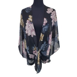May include: Black floral kimono-style top with a tie front. The sheer fabric features a large-scale floral print in shades of pink, blue, and beige. The top is displayed on a black mannequin.
